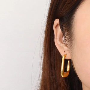 Close-up of gold U-shaped hollow earrings with a polished surface on a model's ear