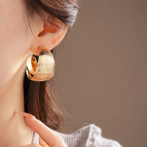 Close-up of golden C-shaped metal hoop earring with a brushed texture on model