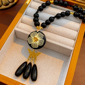 Detail of vintage necklace with black beads, gold flower pendant, butterfly and teardrops