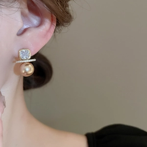 Detailed close-up of gold-plated square zircon and champagne pearl drop earrings on ear