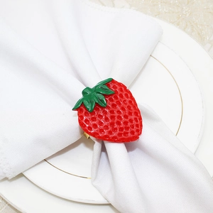 Detailed view of red strawberry napkin ring with green leaves on white napkin and gold plate