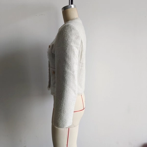 Detail der cremeweißen Tweedjacke mit goldenen Knöpfen und gewebter Fransenstruktur