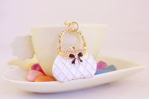Detail of white quilted handbag keychain with sparkling rhinestones and a black bow