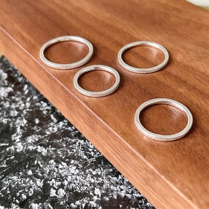 Close-up of four S925 sterling silver rings with vertical texture on a wooden block