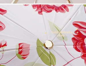 Close-up of golden metal umbrella cap on a white floral print canopy detail