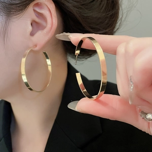 Detailed view of wide flat gold hoop earrings featuring a polished metallic surface