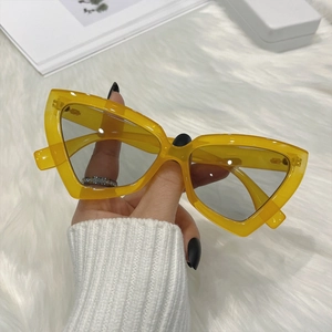 Detail of yellow cat-eye sunglasses with translucent frames held by a hand in white knit