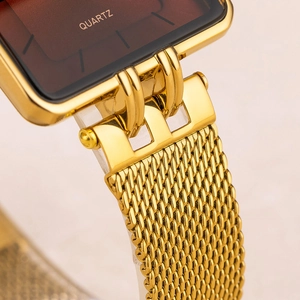Detail of the golden mesh strap connection and polished square quartz watch case