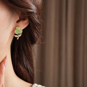 Close-up of gold-plated floral earrings with green petals and zircon leaf on ears