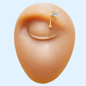 Macro shot of gold curved barbell jewelry with heart-shaped gemstone on eyebrow model
