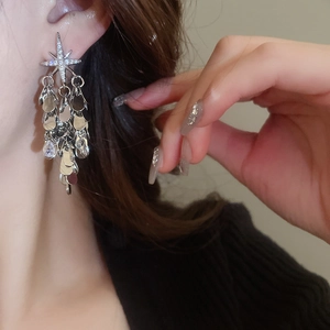 Gros plan de boucles d'oreilles pendantes avec étoile et pompon portées par un mannequin