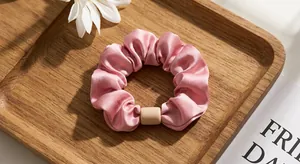 Detail of pink pleated satin scrunchie with apricot resin buckle on a wooden tray