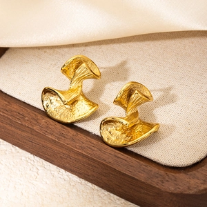 Detailed macro view of gold-plated twisted flower earrings with hammered texture on linen