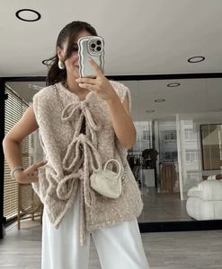 Detail of beige faux fur knitted vest featuring a large bow tie closure design