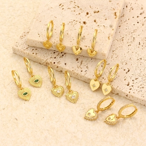 Elegant gold heart earrings set with diamonds and green gemstones on a natural stone base