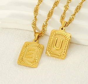 Detail of gold rectangular pendants with embossed letters E and U on twisted chains