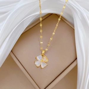 Macro detail of gold clover necklace with zircon and mother of pearl on silk fabric