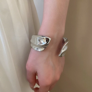 Close-up of silver irregular wavy metal cuff bracelet on model wrist showing sleek texture