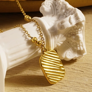 Macro shot of gold rectangle pendant with wavy texture and beaded chain on plaster