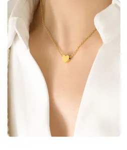 Close-up of a polished gold heart pendant necklace worn on a model in a white shirt