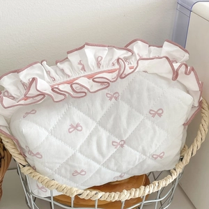 Quilted makeup bag with pink bow pattern and ruffled edge in a rustic metal basket
