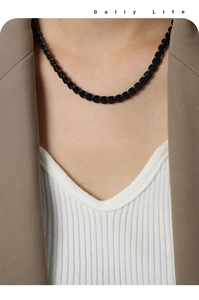 Detail of a minimalist black link chain necklace worn with a chic blazer and white top