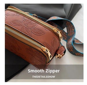 Detailed macro view of the embossed floral leather and smooth gold-tone zippers