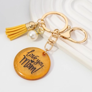 Porte-clés doré avec disque MOM en résine, pompon jaune et perle sur fond blanc