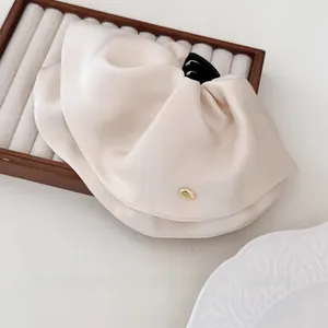 Detailed close-up of cream satin hair claw clip with golden metal logo on wooden tray