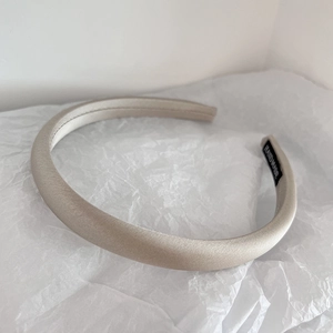 Detail of beige satin headband with silky texture and handmade label on white paper