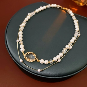 Detail of double-layer necklace with pearls, gold chain, and oval gemstone on stand