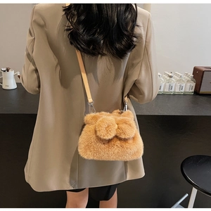 Detailed view of the brown plush bucket bag with pom-pom accents on a model in a cafe