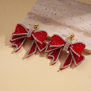 Close-up of red rhinestone bow earrings with gold studs on a textured stone surface