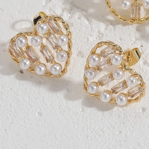 Gros plan d'une boucle d'oreille cœur dorée avec perles et zircons sur pierre blanche