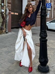 Detail of high-waist white pleated maxi skirt with side slit and black cropped shirt