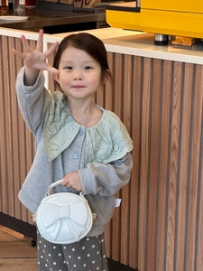 Close-up of a little girl carrying a white round handbag with a cute bow detail