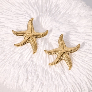 Boucles d'oreilles étoile de mer dorées avec texture martelée sur corail blanc