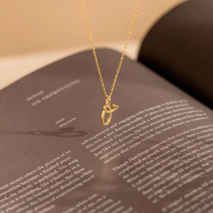 Detail of gold cursive letter O pendant necklace over a vintage book background