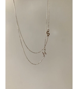 Detailed macro view of minimalist S and H letter pendants on a silver layered necklace