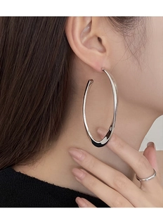 Macro view of model wearing oversized polished silver oval hoop earrings and a matching ring
