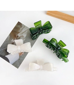 Macro shot of large acetate bow hair claws in glossy dark green and pearl white colors