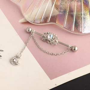 Detail of silver industrial barbell earring with rhinestone lotus and moon chain charm