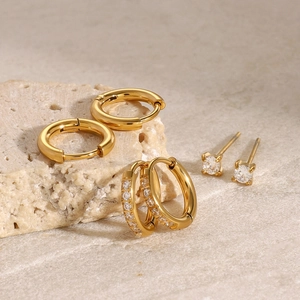 Close-up of gold stainless steel hoop earrings and zircon studs on light mineral stone