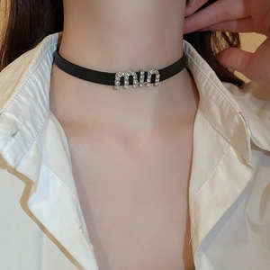 Close-up of a black leather choker featuring a sparkling rhinestone letter logo pendant
