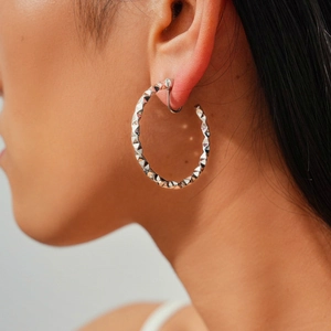 Close-up of a silver geometric textured hoop ear clip on a model showing fine metallic details