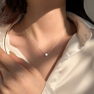 Detailed view of a minimalist cube pendant necklace on neck with warm lighting effect