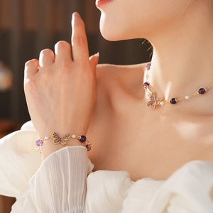 Close-up of butterfly jewelry set with purple stones and pearls on model neck and wrist