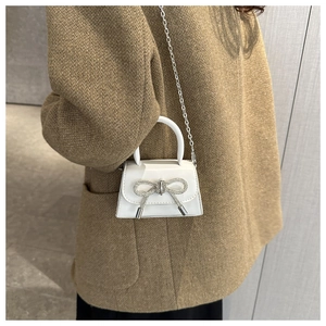 Close-up of a mini white crossbody bag with sparkling rhinestone bow and silver chain strap