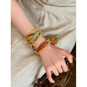 Close-up of vintage gold cuff bracelets with colorful artistic prints on a beige fabric