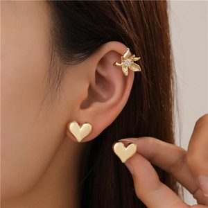 Close-up of a golden flower ear cuff with crystal and heart stud earrings on ear